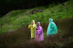 grupo de amigos en impermeables con mochilas en un caminata en el bosque, preparar a excursionismo después el lluvia tiene interrumpido. foto