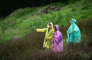 grupo de amigos en impermeables con mochilas en un caminata en el bosque, preparar a excursionismo después el lluvia tiene interrumpido. foto