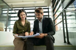 Both of businessperson sitting on stairs in office talk and exchange ideas on using natural energy in buildings before entering the meeting to present and consider photo