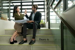 Both of businessperson sitting on stairs in office talk and exchange ideas on using natural energy in buildings before entering the meeting to present and consider photo