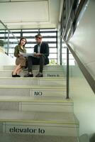 Both of businessperson sitting on stairs in office talk and exchange ideas on using natural energy in buildings before entering the meeting to present and consider photo