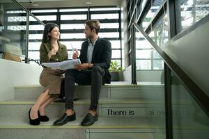 Both of businessperson sitting on stairs in office talk and exchange ideas on using natural energy in buildings before entering the meeting to present and consider photo