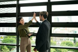 Businessman and businesswoman giving high five while standing by window in office photo