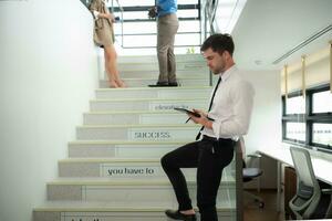 Portrait of young businessman using digital tablet while standing on stairs in office building photo