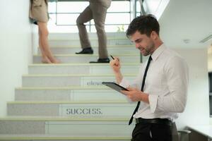 Portrait of young businessman using digital tablet while standing on stairs in office building photo