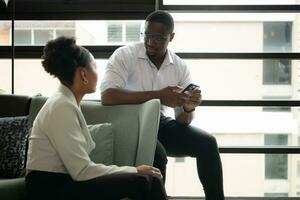 joven africano americano mujer de negocios hablando con su jefe mientras sentado en sofá en oficina foto
