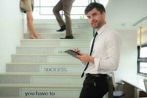Portrait of young businessman using digital tablet while standing on stairs in office building photo