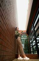 Portrait of a beautiful young woman drinking coffee and using mobile phone while leaning on a brick wall photo