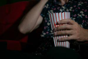 Young man watching movie and eating popcorn while sitting on red couch photo