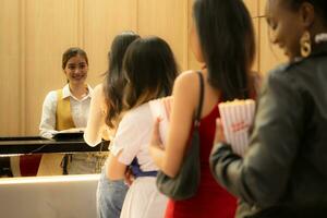 Young asian woman standing in line to buy movie tickets and in hand popcorn and drink, Smiling ticket salesman serving. photo