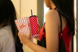 Young asian woman standing in line to buy movie tickets and in hand popcorn and drink photo