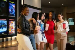 Group of happy friends watching movie in cinema and eating popcorn at night photo