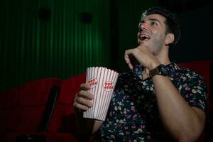 joven hombre acecho película y comiendo palomitas de maiz mientras sentado en rojo sofá foto