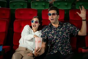 In a cinema, A young couple pair wearing 3D glasses watches movies and eats popcorn. photo