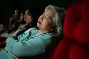 mayor mujer caídas dormido mientras acecho película en cine y palomitas de maiz en mano, película carente interesante y aburrido. foto