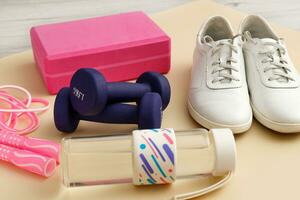 sneakers, jump rope, water bottle, dumbbells and a yoga brick on a light background photo