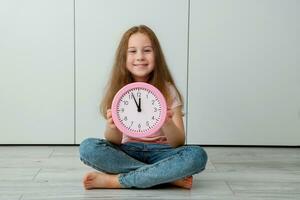 niña sentado en el piso participación un reloj ese muestra 5 5 minutos a 12 foto