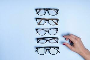 Eyeglasses and female hand on blue background. Optical store, vision test, stylish glasses concept top view photo