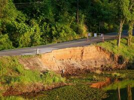 Asphalt road destroyed by the landslide, Asphalt road collapsed with cracks and hole in sunny day, Destroyed edge of asphalt pavement in the countryside. Destruction of road caused by flood water photo