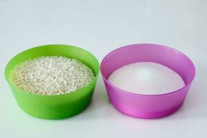 vistoso ingredientes. púrpura y verde el plastico bochas con arroz y azúcar para cremoso arroz pudín, en blanco antecedentes foto