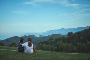 A couple of brothers hugging each other contemplate a beautiful green mountain landscape and coastal cliffs in the background photo