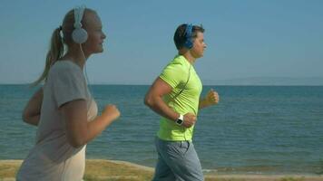 couple dans écouteurs le jogging le long de le mer de face video