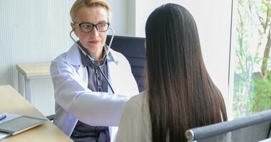 Asian woman patient sitting with doctor about her illness and showing x-ray results with blood pressure and heart rate measurement with stethoscope photo