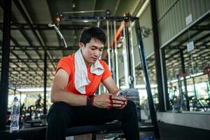 young male playing phone and listening to music after exercise with various exercise equipment in fitness. photo