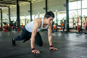 man doing mountain climbing in the gym. a man raising his legs up and moving in the air. Health care in fitness gym concept. photo