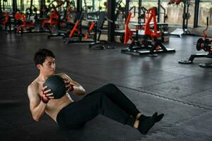 muscular man exercising with a pilates ball at the gym. Male sitting on the floor and doing a workout using a medicine ball. photo