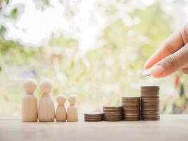 Close up hand putting coins to stack of coins with wooden human figure for saving concept photo