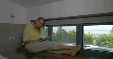 leende kvinna med läsplatta på fönster tröskel video