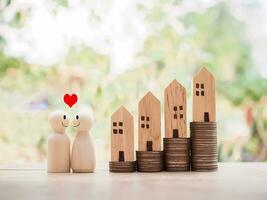de madera figura Pareja contento cara con corazón y miniatura casa en apilar de monedas para inversión propiedad concepto. ahorro dinero para comprar un casa. foto