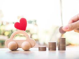 Close up of hand putting coins in stack of coins and wooden toy car for transport and manage success business concept. Concept of car loan photo