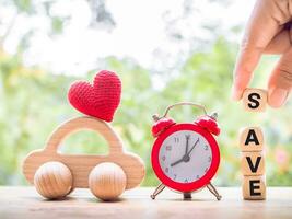 Close up hand holding wooden block with word SAVE, wooden toy car and red alarm. The concept of saving for car. photo