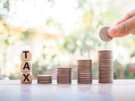 Close up hand putting coin in stack of coins, Wooden blocks with the word TAX. The concept of save money for paying tax in the future photo