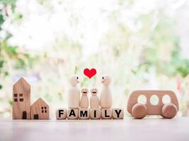 Wooden figure of the family standing on wooden blocks with the word FAMILY, wooden toy car and miniature house for happy family concept photo