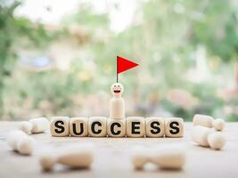 Wooden human figure on top of wooden block with the word SUCCESS and red flag. Human Resource Development concept. Goals achievement and business success. photo