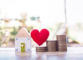 Miniature house, red heart and stack of coins. Investment property concept. photo