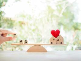 Close up hand holding wooden block with word TAX and miniature house on balancing scale. The concept of paying tax for house and property. photo