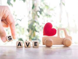 Close up hand holding wooden block with word SAVE, wooden toy car with red heart. The concept of saving for car. photo