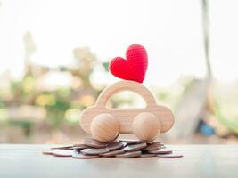 de madera juguete coche con rojo corazón en apilar monedas ahorro dinero para transporte y gestionar para éxito negocio concepto. concepto de coche préstamo foto