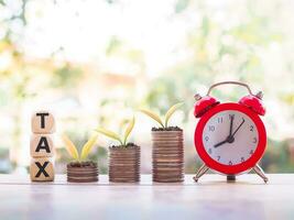 Plants growing up on stack of coins, Red alarm and wooden blocks with the word TAX. The concept of paying tax for every thing. photo