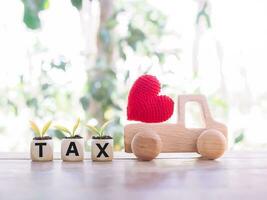 Red heart on wooden toy car and wooden blocks with the word TAX. The concept of paying tax for car. Car taxes. photo