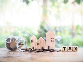 Miniature house on stack of coins and wooden blocks with the word TAX. The concept of paying tax for house and property. Property taxes. photo