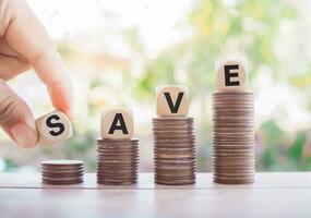 Close up hand holding wooden block with word SAVE on stack of coins. The concept of paying tax for everthing. photo