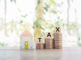 Miniature house and wooden blocks with the word TAX on stack of coins. The concept of paying tax for house and property. Property taxes. photo