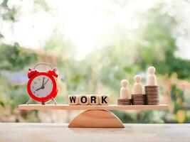 Wooden human figure standing on stack of coins, red alarm and wooden block with the word WORK on balancing scale. photo