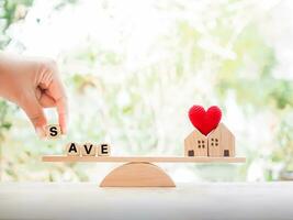 Close up hand holding wooden block with word SAVE and miniature house on balancing scale. The concept of paying tax for house and property. photo