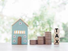 Miniature house, wooden blocks with the word TAX and stack of coins. The concept of paying tax for house and property. photo